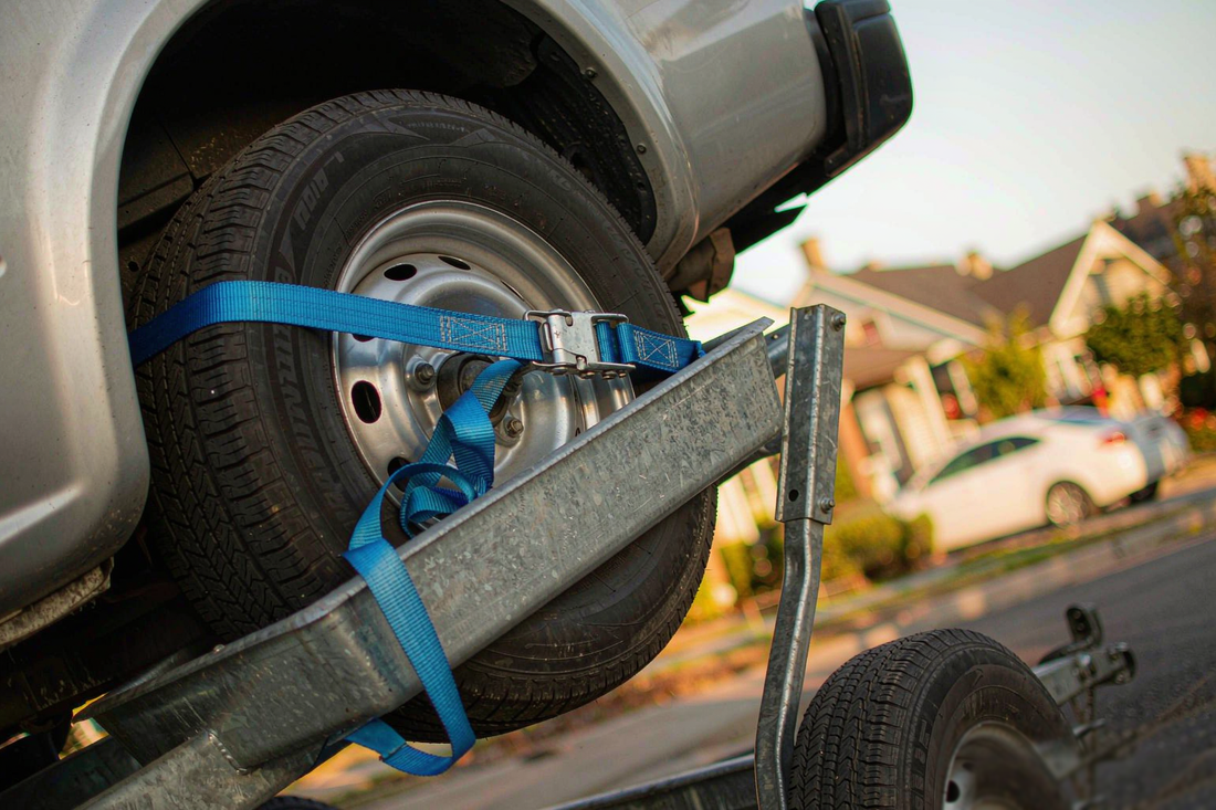 Blue basket strap securing a car tire seated in the steel pan of a two-wheel tow dolly