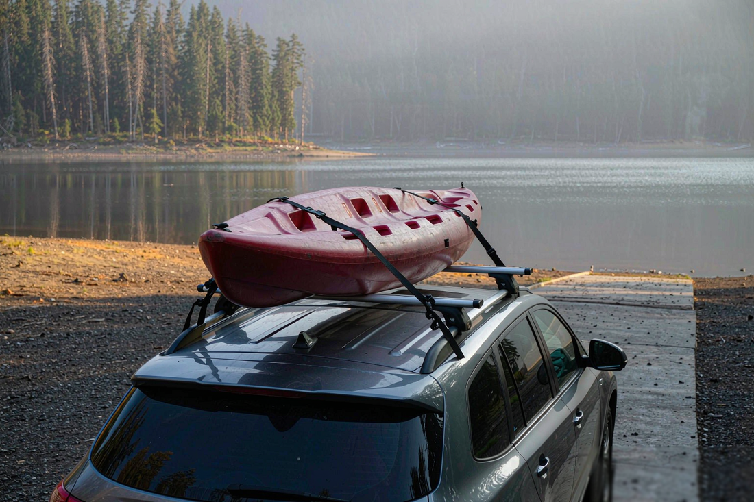Kayak tied to a car roof rack with two 1 inch retractable ratchet straps running over the deck