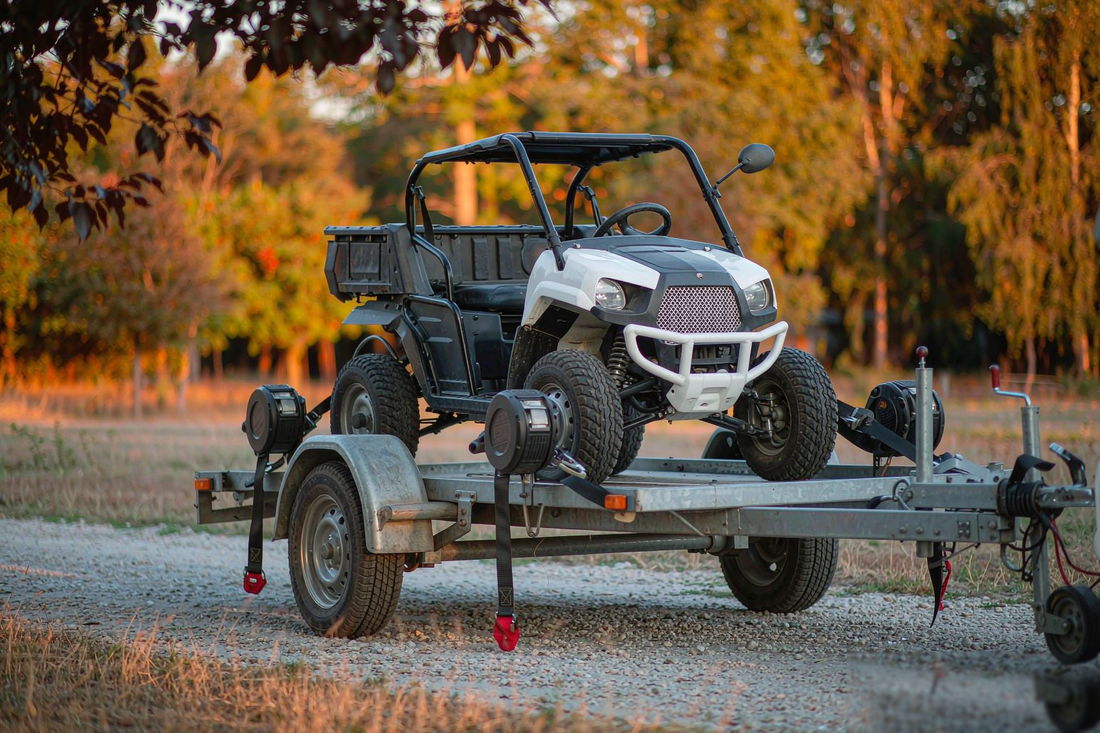 Retractable ratchet straps securing a side-by-side UTV on a utility trailer at golden hour