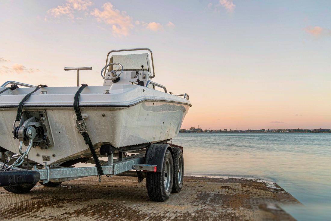 White fishing boat on a trailer at a boat ramp secured with black tie down straps